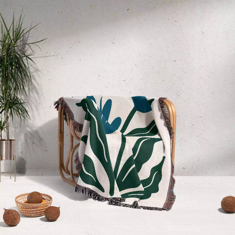 Matisse inspired blue flowers woven throw blanket with green leaf pattern draped over a chair against a light gray wall.