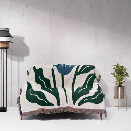 Floral-patterned Matisse inspired blue flowers woven throw blanket draped over a chair against a white wall.