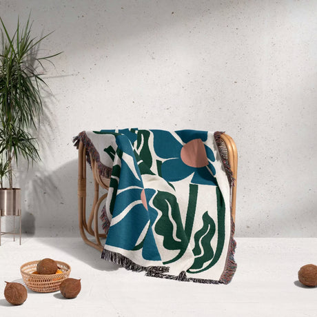 Decorative Matisse style blue flowers cotton woven throw blanket with floral pattern on a chair against a white wall.