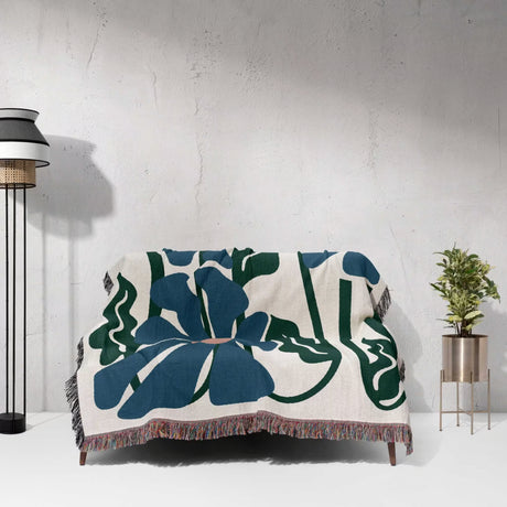 Decorative Matisse style blue flowers cotton woven throw blanket with blue and green floral pattern draped over a chair against a white wall.