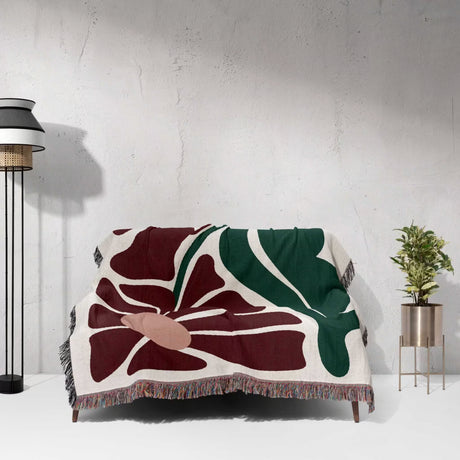 Decorative Matisse style botanical cotton woven throw blanket with abstract design draped over a chair against a white wall.