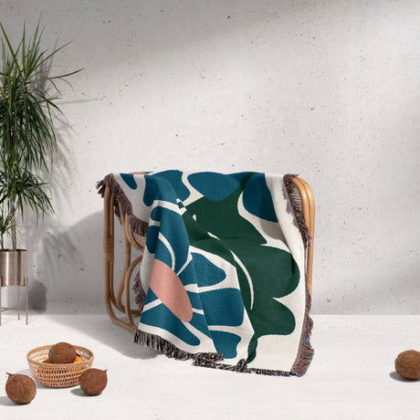 Decorative Matisse style floral cotton woven throw blanket for couch with leaf pattern draped over a chair against a light gray wall.