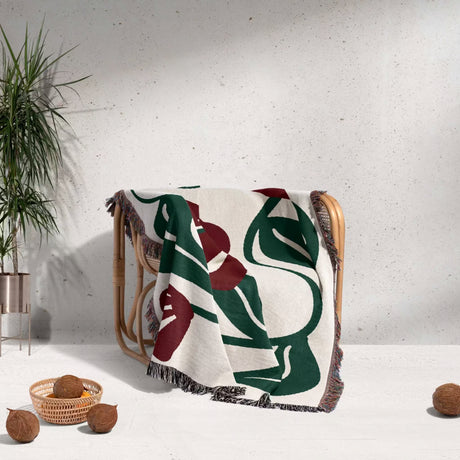 Decorative Matisse style red floral cotton woven throw blanket with leaf pattern draped over a chair against a light gray wall.