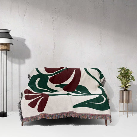 Decorative Matisse style red floral cotton woven throw blanket with a floral pattern draped over a chair against a white wall.
