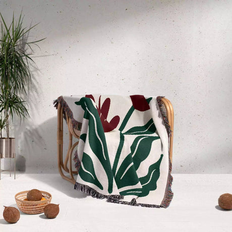 Floral-patterned Matisse style red flowers woven throw blanket draped over a chair against a white wall with decorative elements.