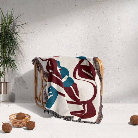 Decorative Matisse style red and blue cotton woven throw blanket with abstract patterns draped over a chair against a light background