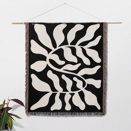 Black leaf Matisse throw blanket as woven wall art hanging with abstract leaf pattern on a black background, hanging on a white wall.