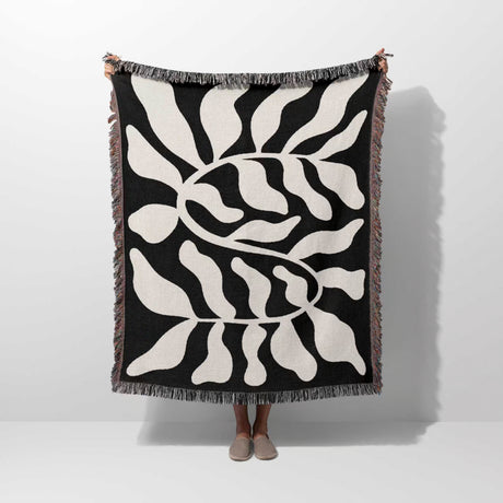 Black leaf Matisse throw blanket held up by a person on a white background