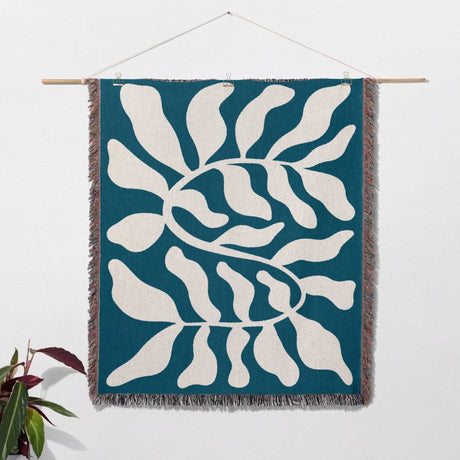 Blue leaf abstract woven Matisse trow blanket tapestry as woven wall art hanging on a white wall.