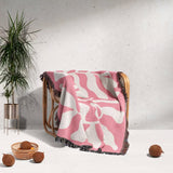 Lighter red abstract Matisse throw blanket draped over a wooden chair with a plant and coconuts in the background.