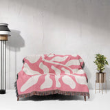 Lighter red abstract Matisse throw blanket draped over a couch against a white wall.