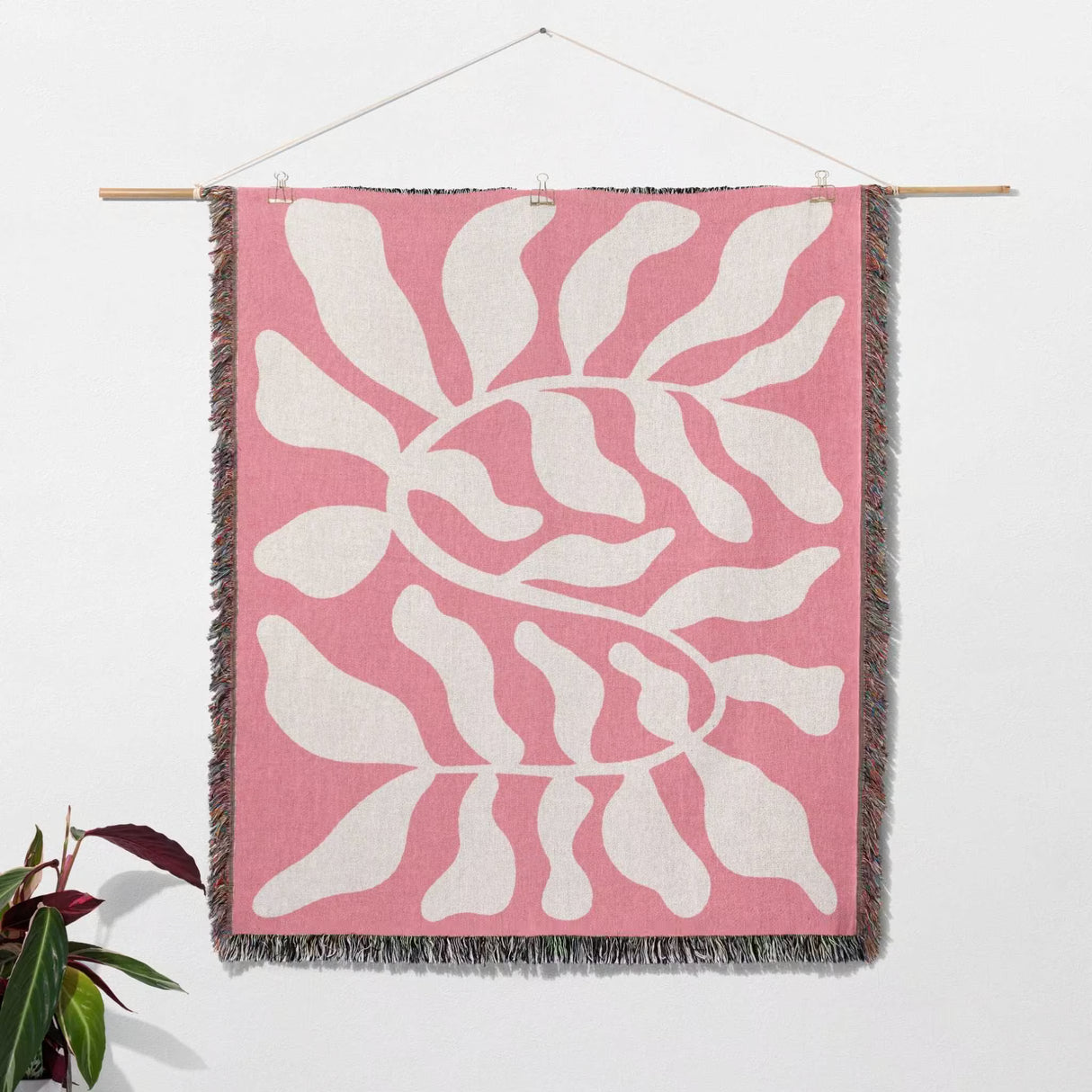 Lighter red abstract Matisse throw blanket with white leaf pattern hanging on a wall on a white background