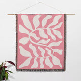 Lighter red abstract Matisse throw blanket with white leaf pattern hanging on a wall on a white background