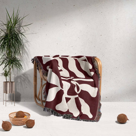 Red leaf abstract Matisse throw blanket draped over a chair against a light gray wall.