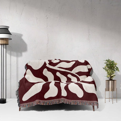 Red leaf abstract Matisse throw blanket draped over a couch against a white wall.