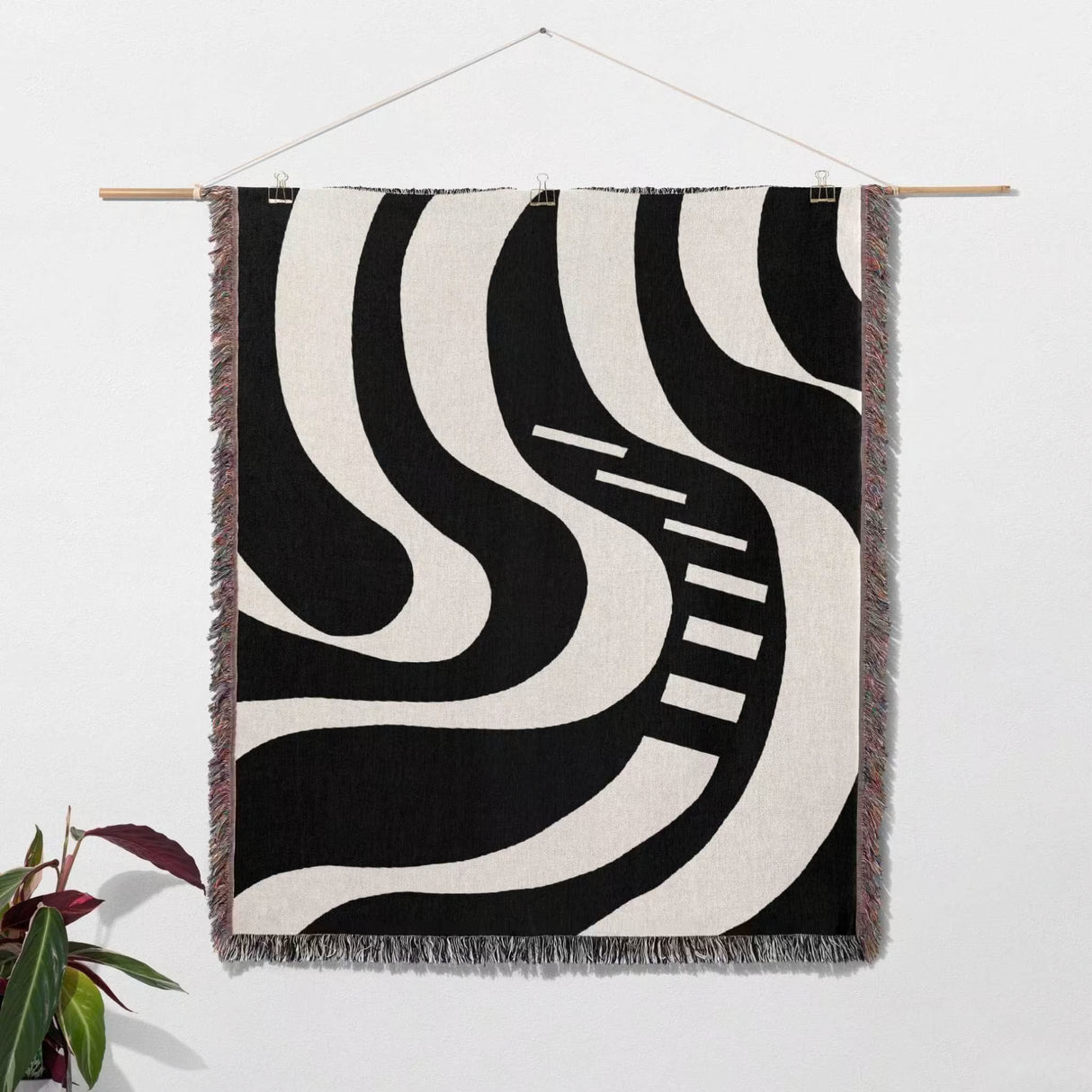 Black and white modern abstract art woven blanket throw tapestry hanging on a wall with a plant in the corner.