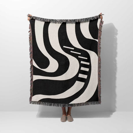 Person holding a black and white modern abstract art woven blanket throw tapestry against a white background.