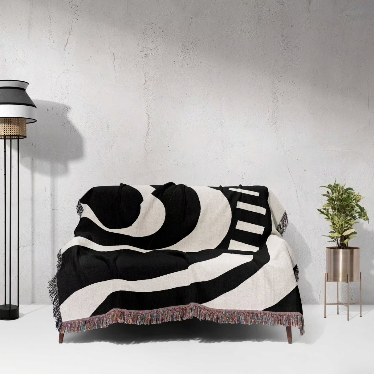Black and white modern abstract art woven blanket throw tapestry draped over a sofa against a white wall.