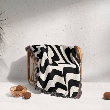 Black and white modern abstract waves woven blanket throw tapestry over a wooden chair against a light gray wall.