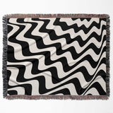 Black and white modern abstract waves woven blanket throw tapestry flat lay on a beige background.