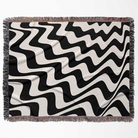 Black and white modern abstract waves woven blanket throw tapestry flat lay on a beige background.