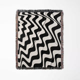 Black and white modern abstract waves woven blanket throw tapestry flat lay on a light gray background.