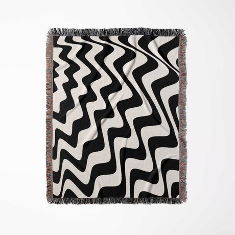 Black and white modern abstract waves woven blanket throw tapestry flat lay on a light gray background.