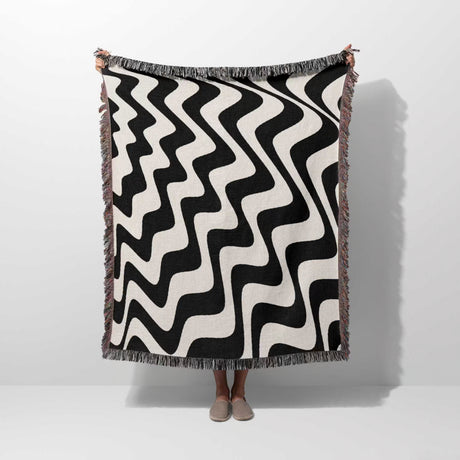 Black and white modern abstract waves woven blanket throw tapestry held by a person on a white background.