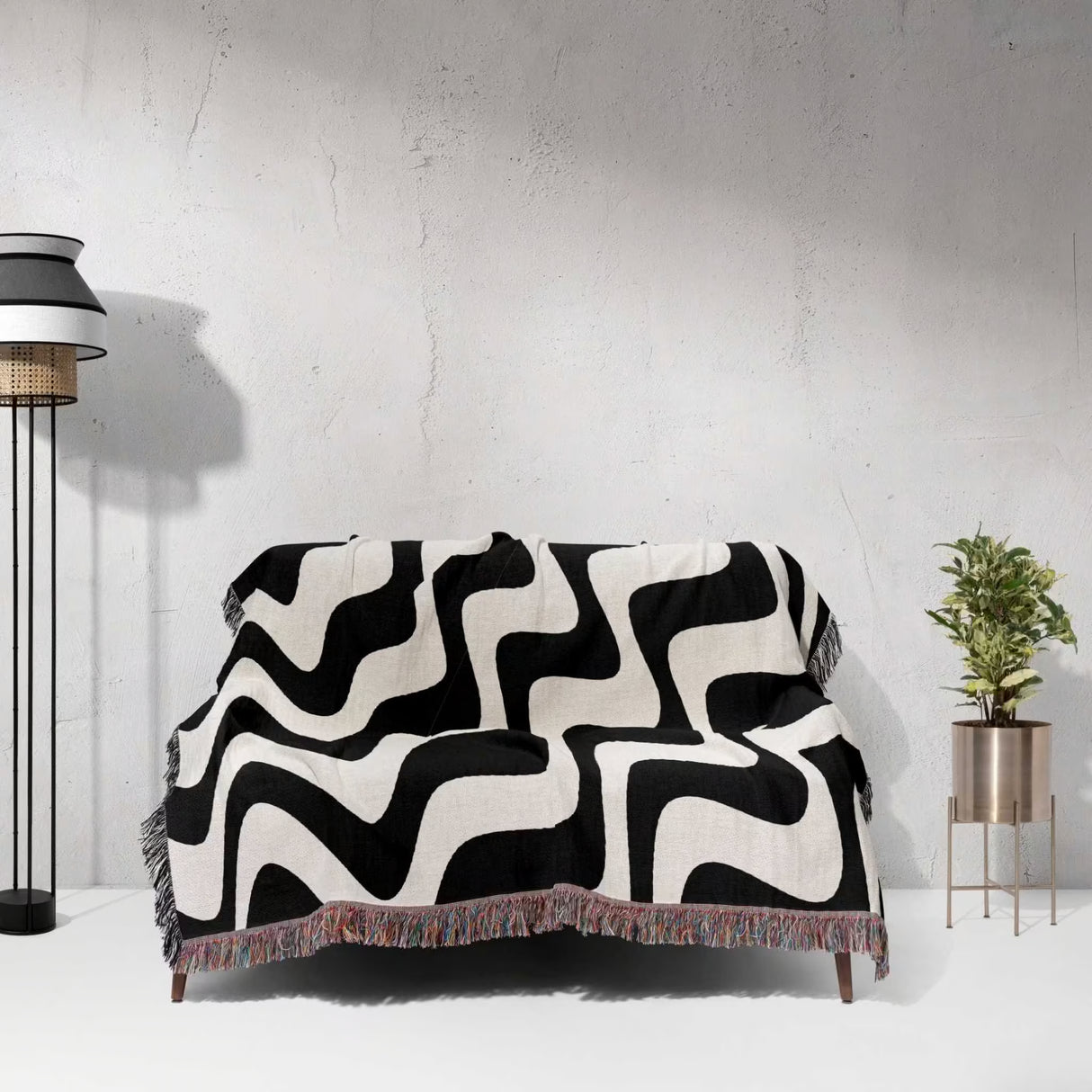 Black and white modern abstract waves woven blanket throw tapestry draped over a sofa against a light gray wall.