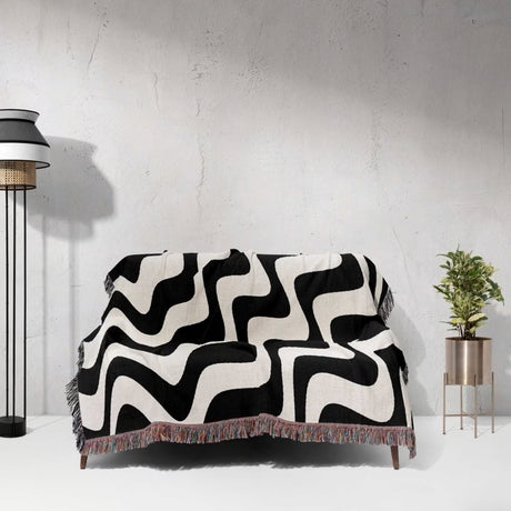 Black and white modern abstract waves woven blanket throw tapestry draped over a sofa against a light gray wall.