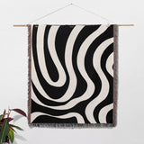Black and white modern abstract woven blanket throw tapestry hanging on a wall with a plant in the corner.