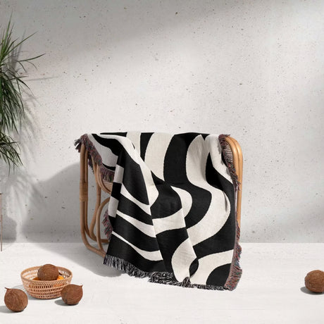 Black and white modern abstract woven blanket throw tapestry draped over a chair against a light gray wall.