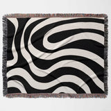 Black and white modern abstract woven blanket throw tapestry with fringed edges flat lay on a light gray background