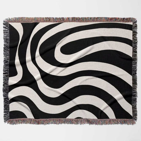 Black and white modern abstract woven blanket throw tapestry with fringed edges flat lay on a light gray background
