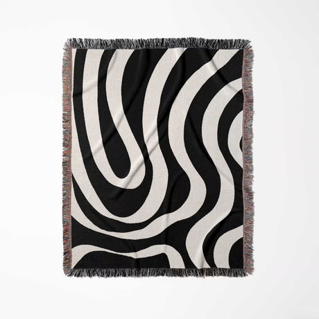 Black and white modern abstract woven blanket throw tapestry with fringe full view on a light gray background