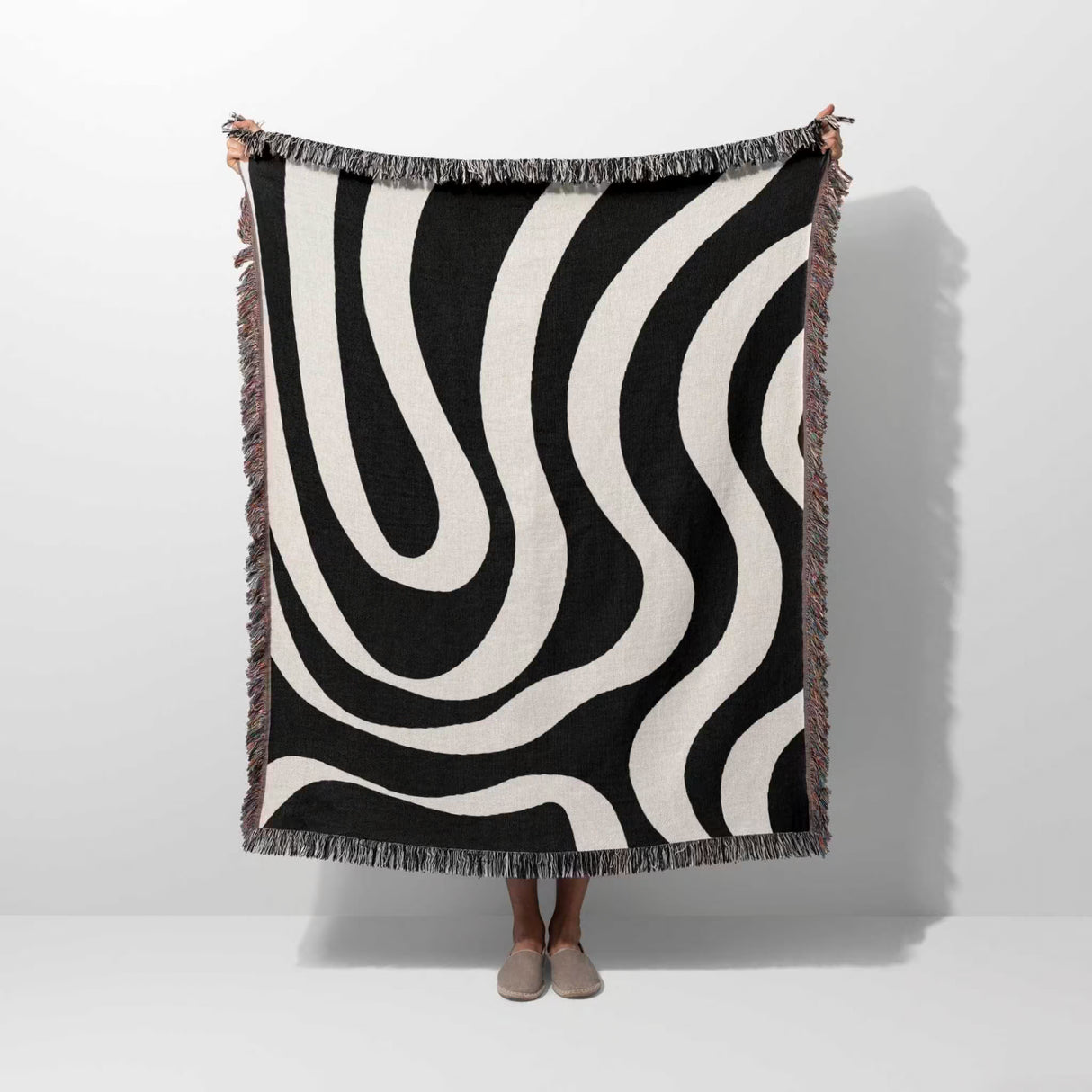 Black and white modern abstract woven blanket throw tapestry held by a person on a white background
