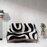 Black and white modern abstract woven blanket throw tapestry on a sofa against a light gray wall.