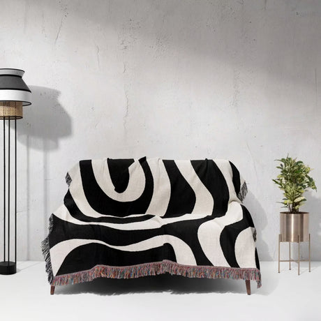 Black and white modern abstract woven blanket throw tapestry on a sofa against a light gray wall.