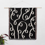 Black and white modern accent woven blanket throw tapestry hanging on a wooden rod against a white wall.