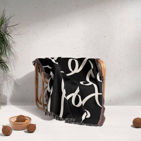 Black and white modern accent woven blanket throw tapestry draped over a chair with a minimal gray background.