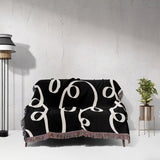 Black and white modern accent woven blanket throw tapestry draped over a couch against a white wall.