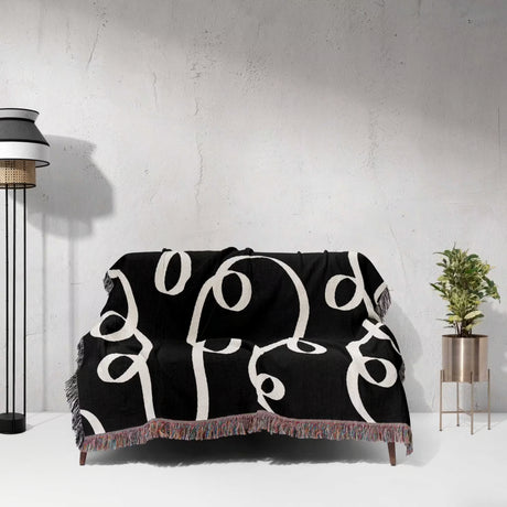 Black and white modern accent woven blanket throw tapestry draped over a couch against a white wall.