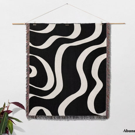 Black and white modern aesthetic waves woven blanket throw hanging on a wooden rod against a white wall.
