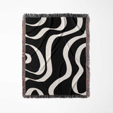 Black and white modern aesthetic waves woven blanket throw with fringed edges flat lay on a light gray background.