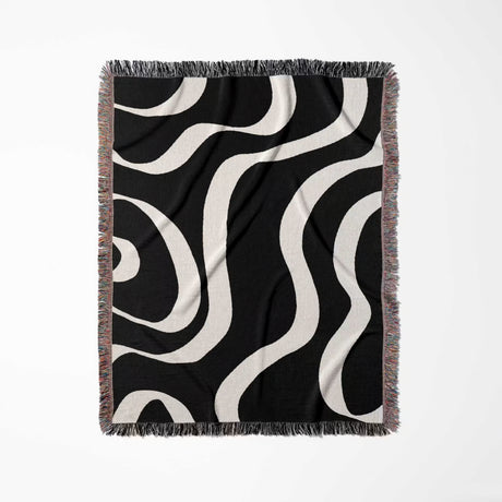 Black and white modern aesthetic waves woven blanket throw with fringed edges flat lay on a light gray background.