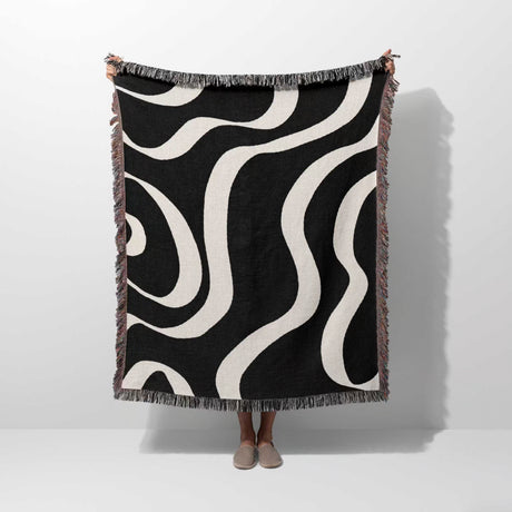 Black and white modern aesthetic waves woven blanket throw held by a person on a white background.