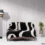 Black and white modern aesthetic waves woven blanket throw draped over a sofa against a white wall.