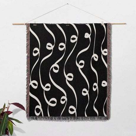 Black and white modern art decorative woven blanket throw tapestry as wall art hanging on a white wall.