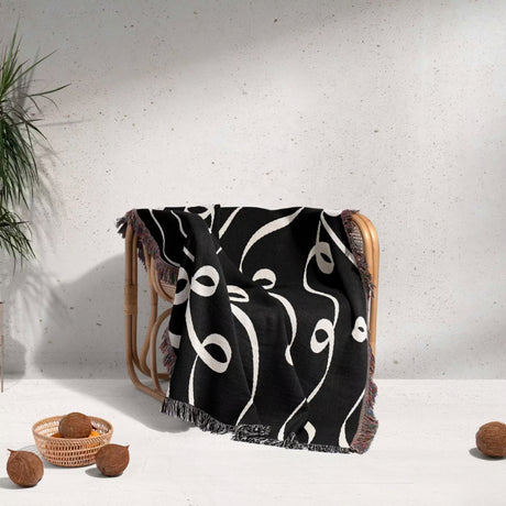Black and white modern art decorative woven blanket throw tapestry draped over a chair against a light gray wall.