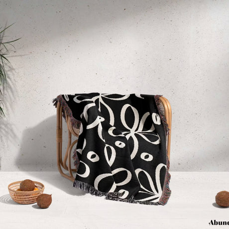 Black and white modern artsy flowers woven blanket throw draped over a chair against a light gray wall.